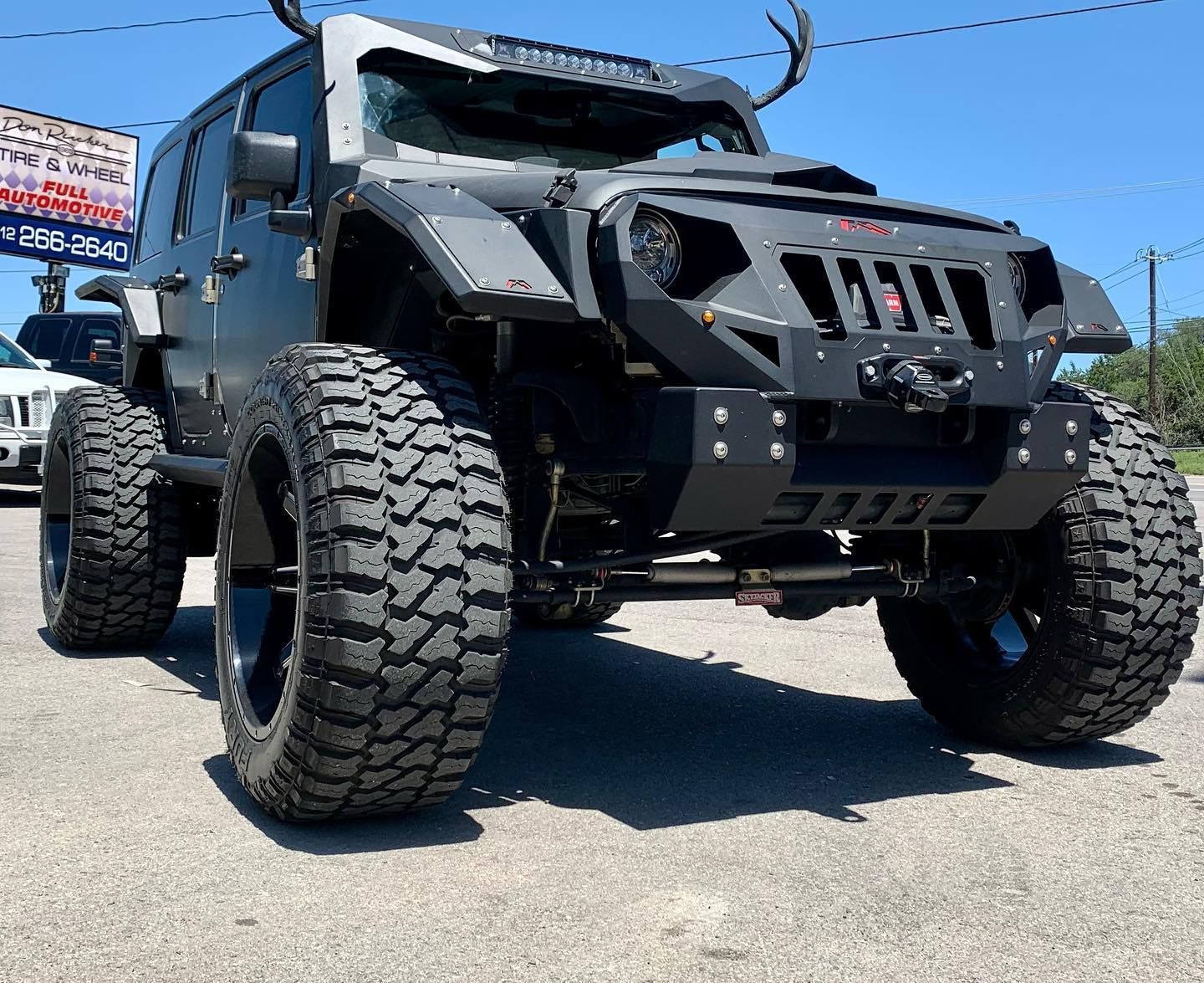 A black jeep is parked in front of a car dealership.