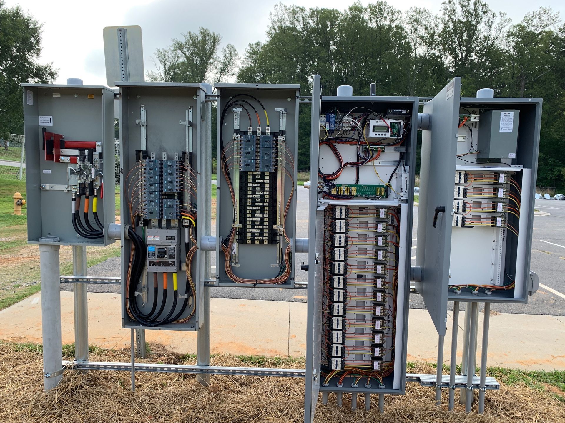 Gray electrical panel boxes with open doors on a metal frame outdoors.