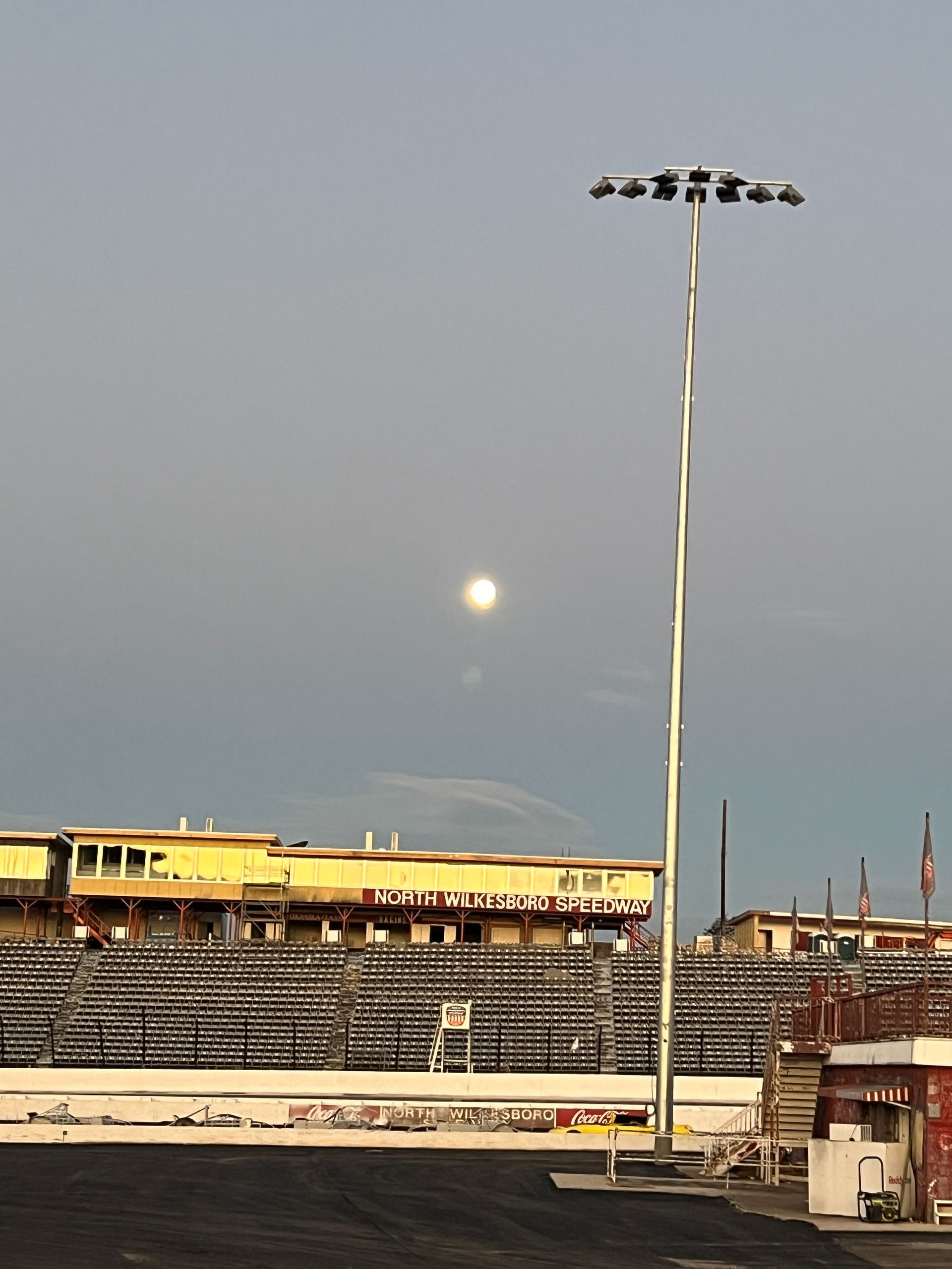 Moonlit stadium with tall light pole. Bleachers, yellow building, dark track.