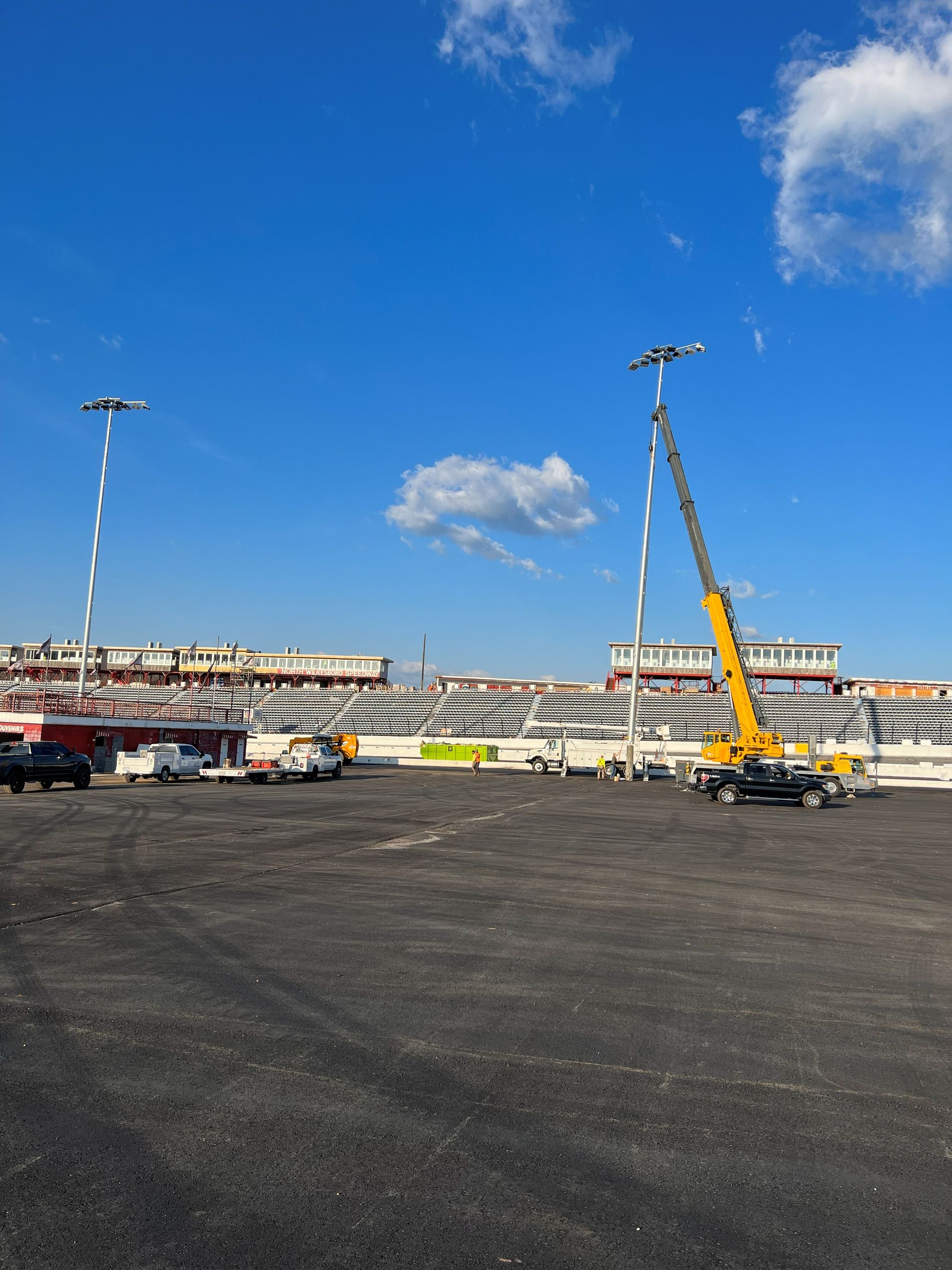 A large, empty parking lot with grandstands and a crane under a blue sky.