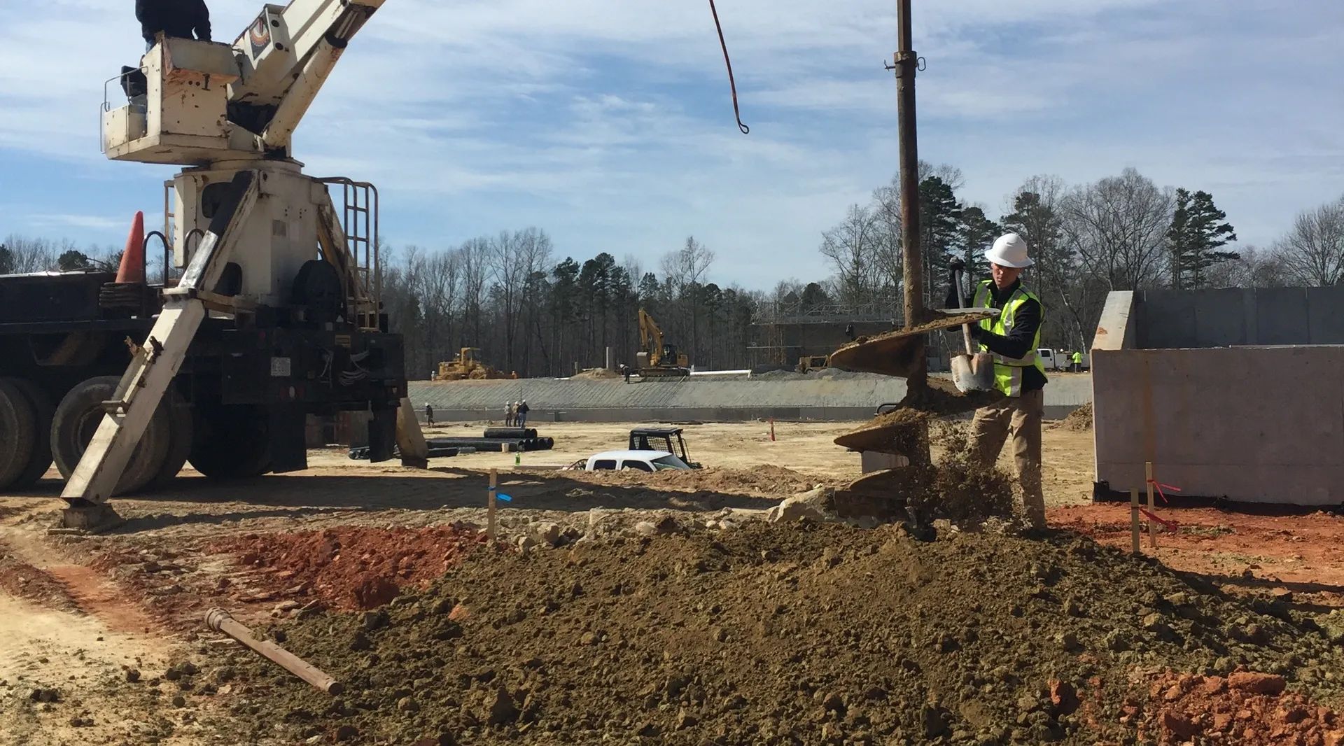 Construction worker using a drill, near a crane, in a dirt area.