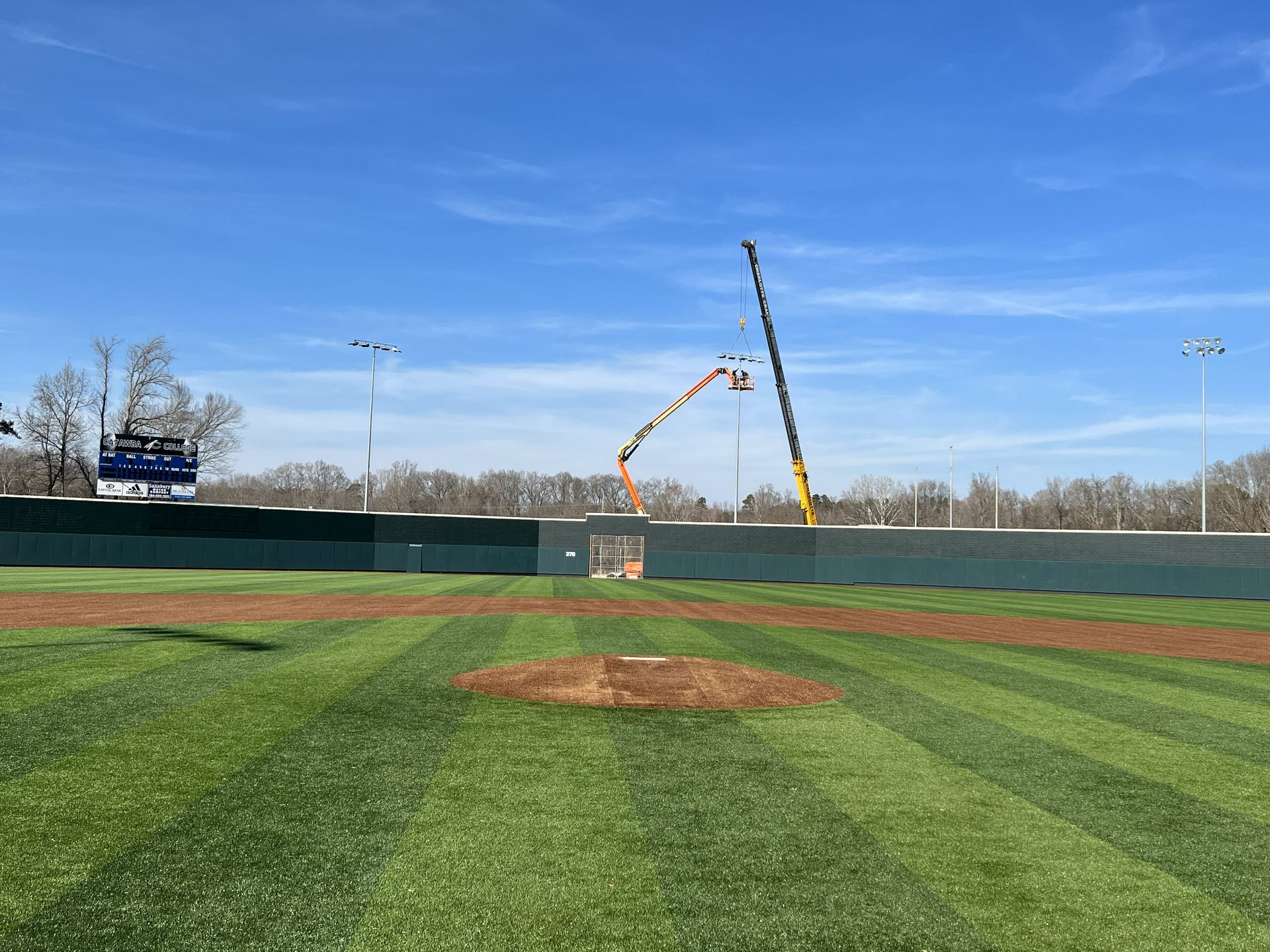 A crane working on power lines near a road. A green trash can sits on the side. Bright blue sky.