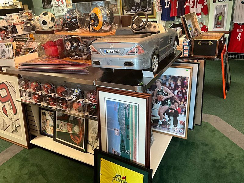 Display of sports memorabilia, framed art, and a toy car in a shop, with green carpet.