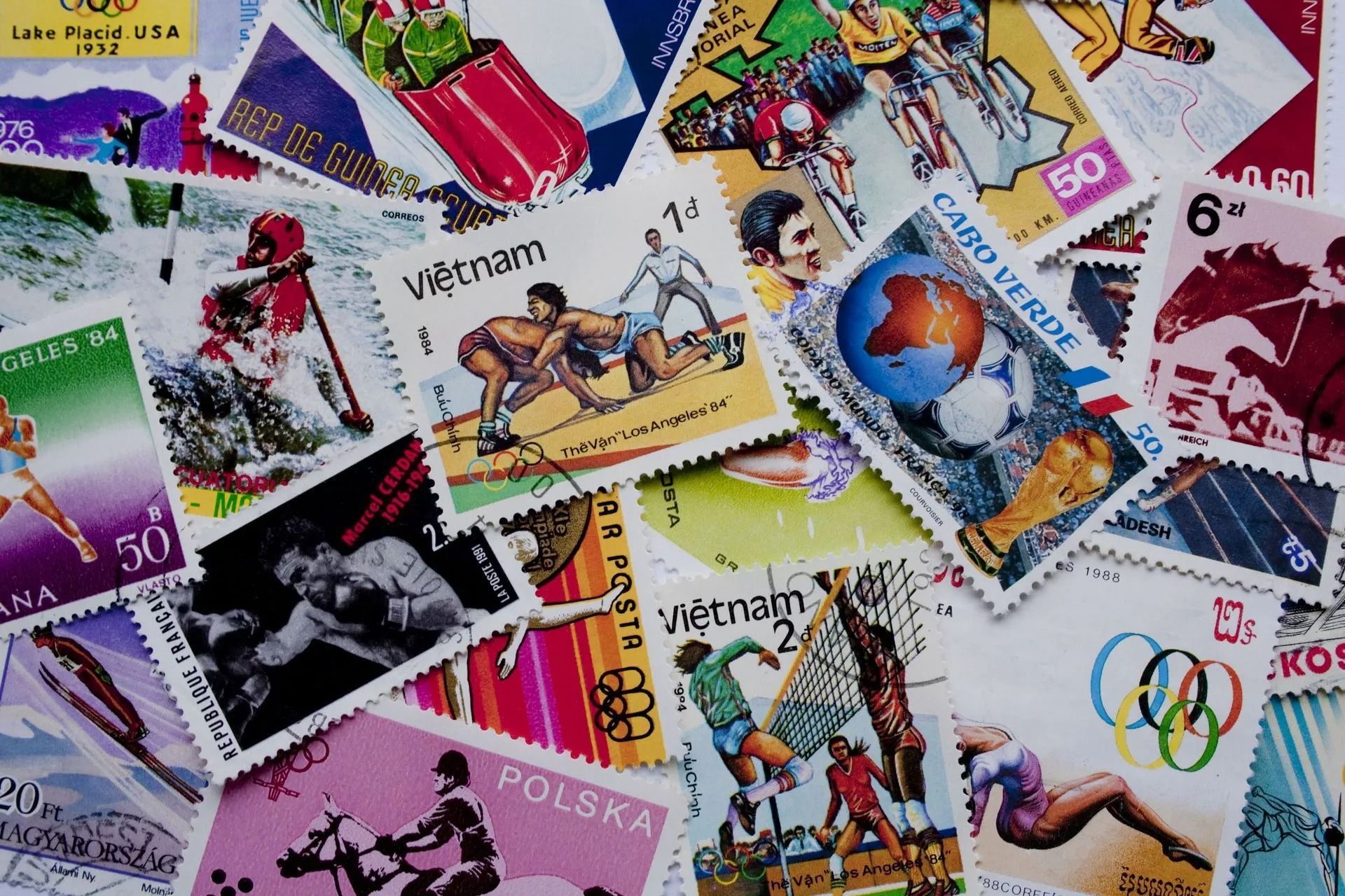 Pile of colorful postage stamps; some feature athletes, a globe, and other designs.