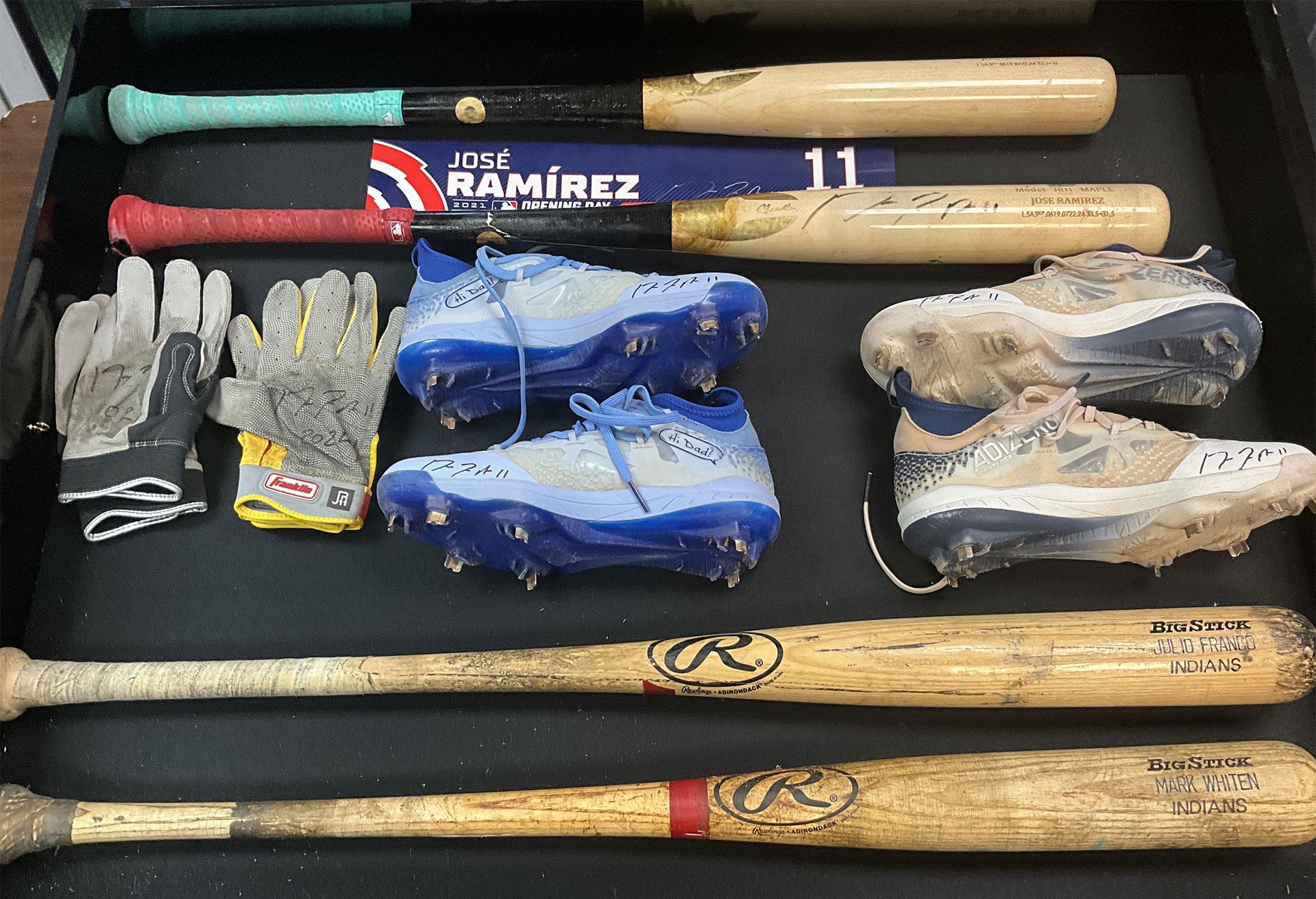 Baseball equipment: bats, gloves, and cleats arranged on a dark surface.