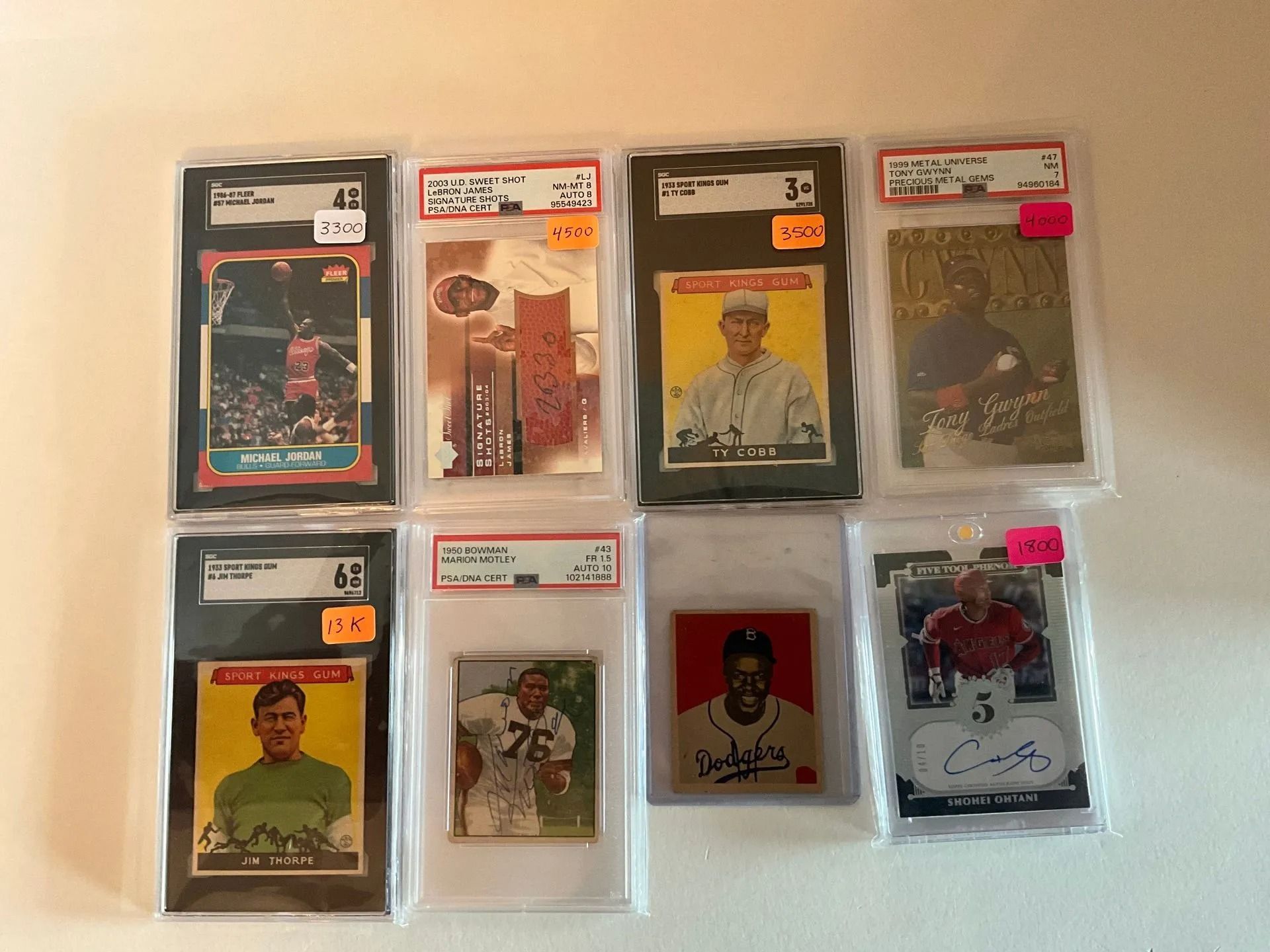 Collection of graded sports trading cards in protective holders, varying sizes and colors, on a white surface.