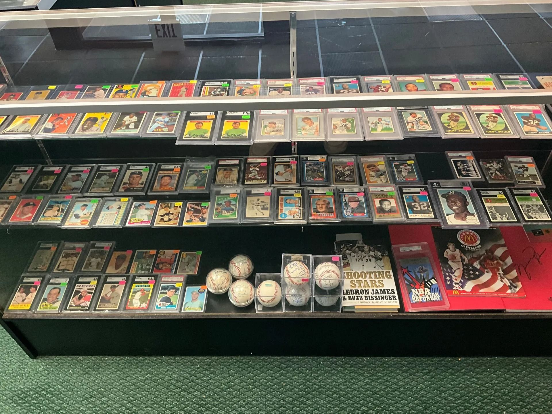 Display case with rows of baseball cards, baseballs, and memorabilia on a green carpet.
