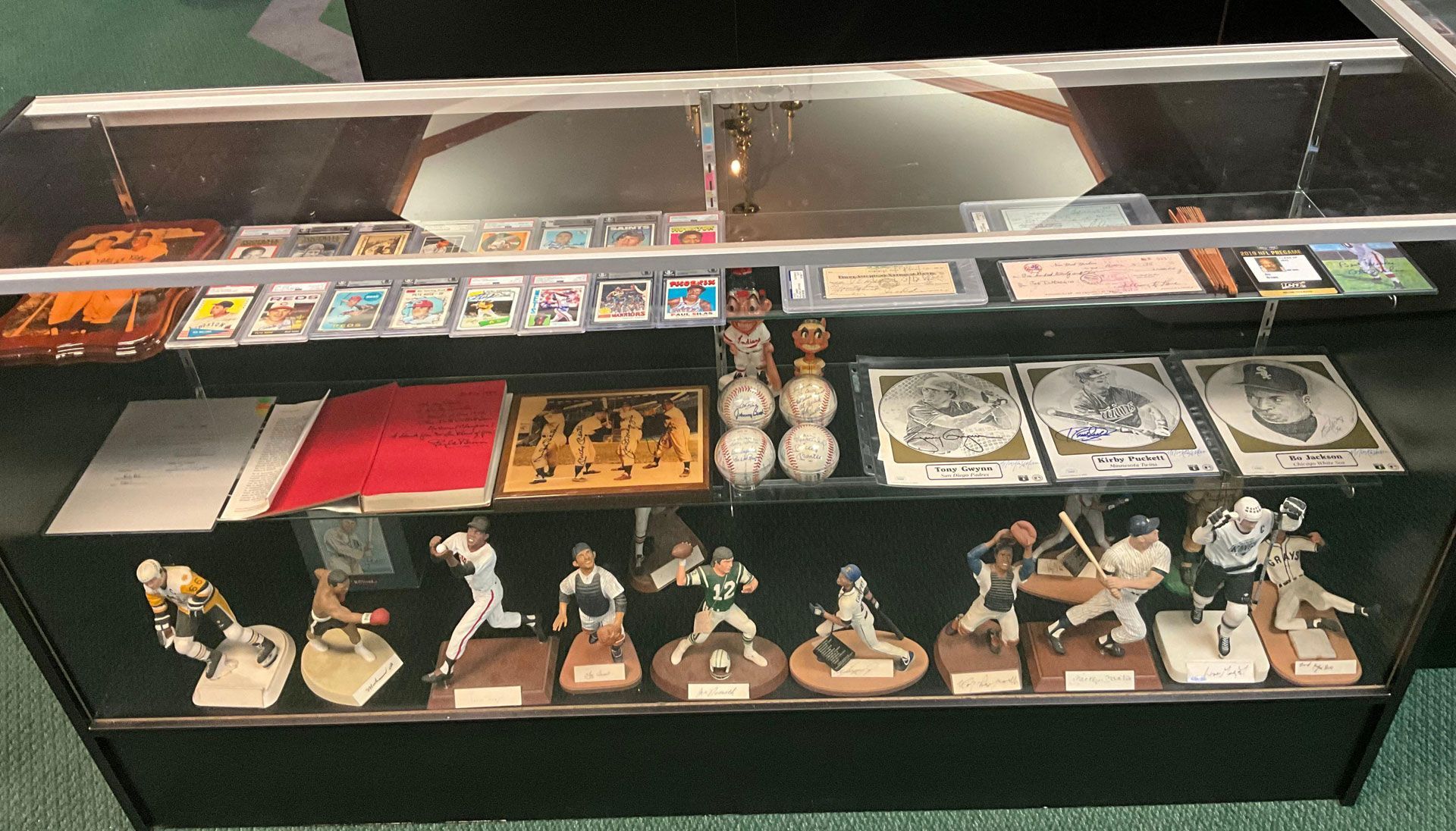 A display case holding baseball memorabilia, including cards, signed balls, figurines, and plaques.