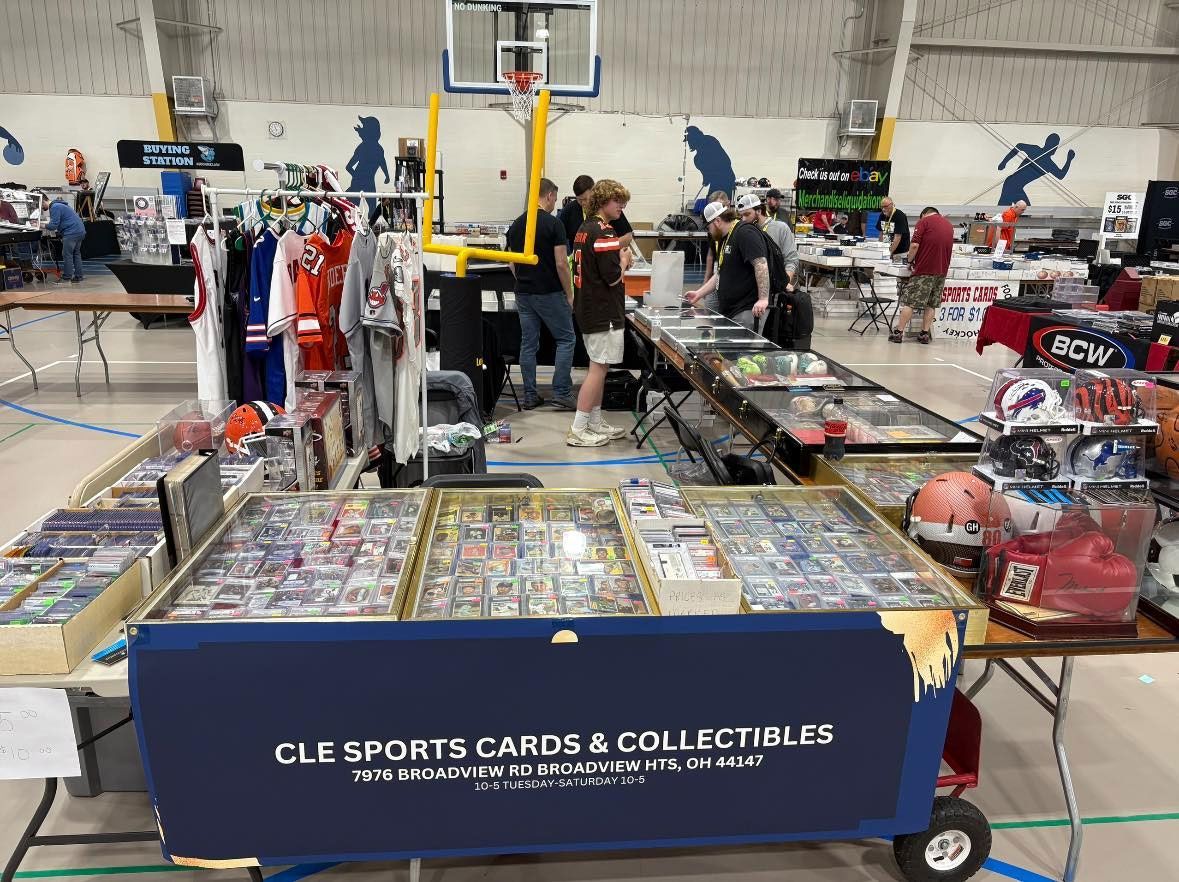 Sports card and memorabilia show: Vendors with tables of cards, jerseys, and other items. People browse and shop.