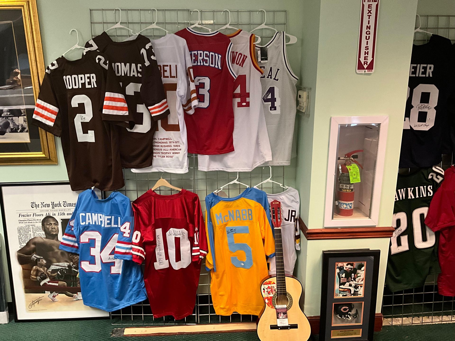 Sports jerseys, a guitar, and memorabilia displayed on a wall in a store.