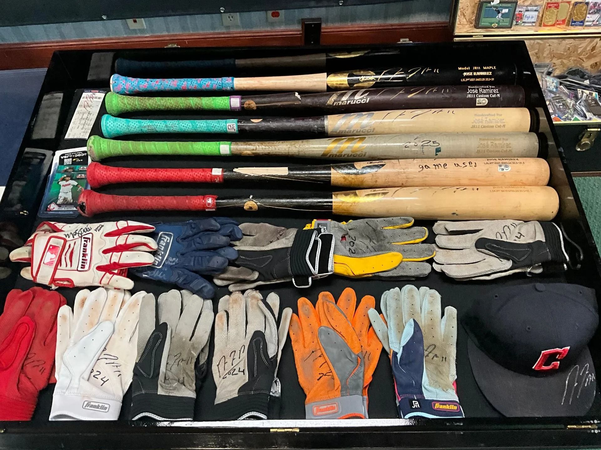 Baseball bats and gloves arranged in a drawer; various colors of grips, gloves signed and a team cap.