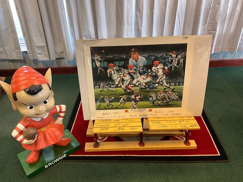 Browns memorabilia: elf statue next to signed football art and miniature benches on a red mat.
