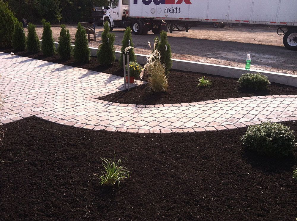 A brick pathway winds through a beautifully landscaped patio with trees around it.