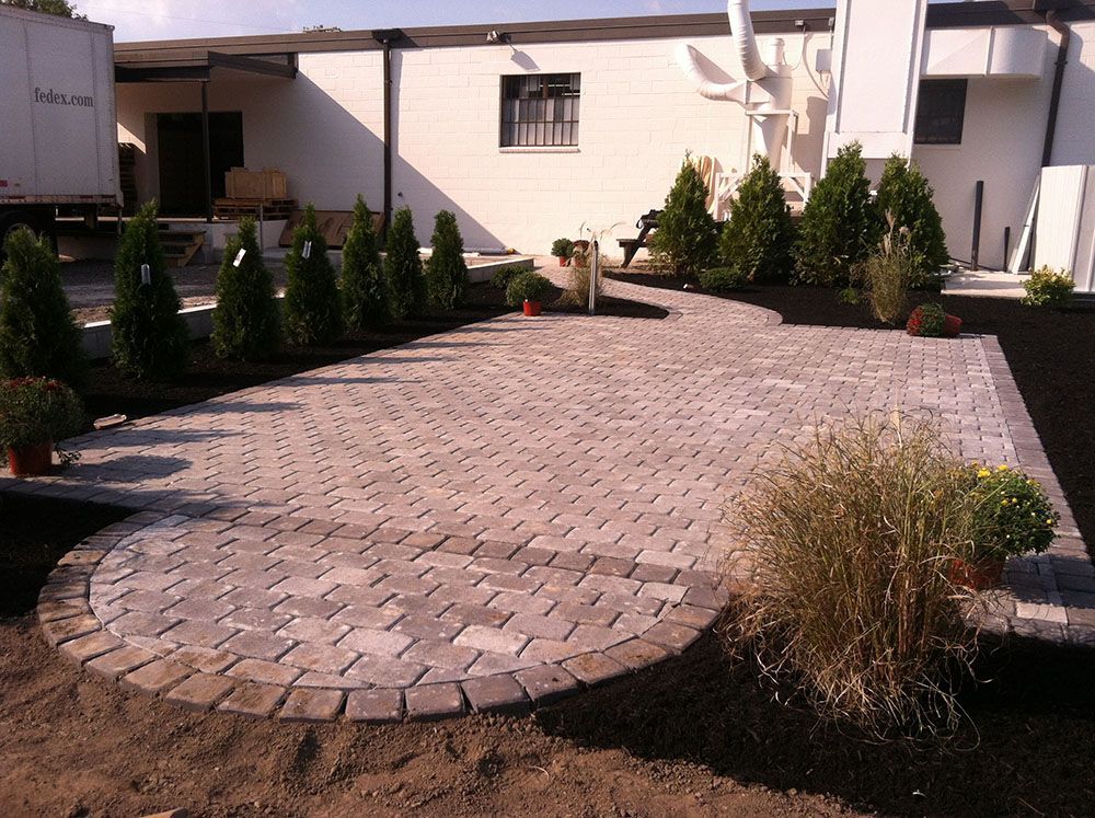 A brick pathway winds through a beautifully landscaped patio surrounded by trees.