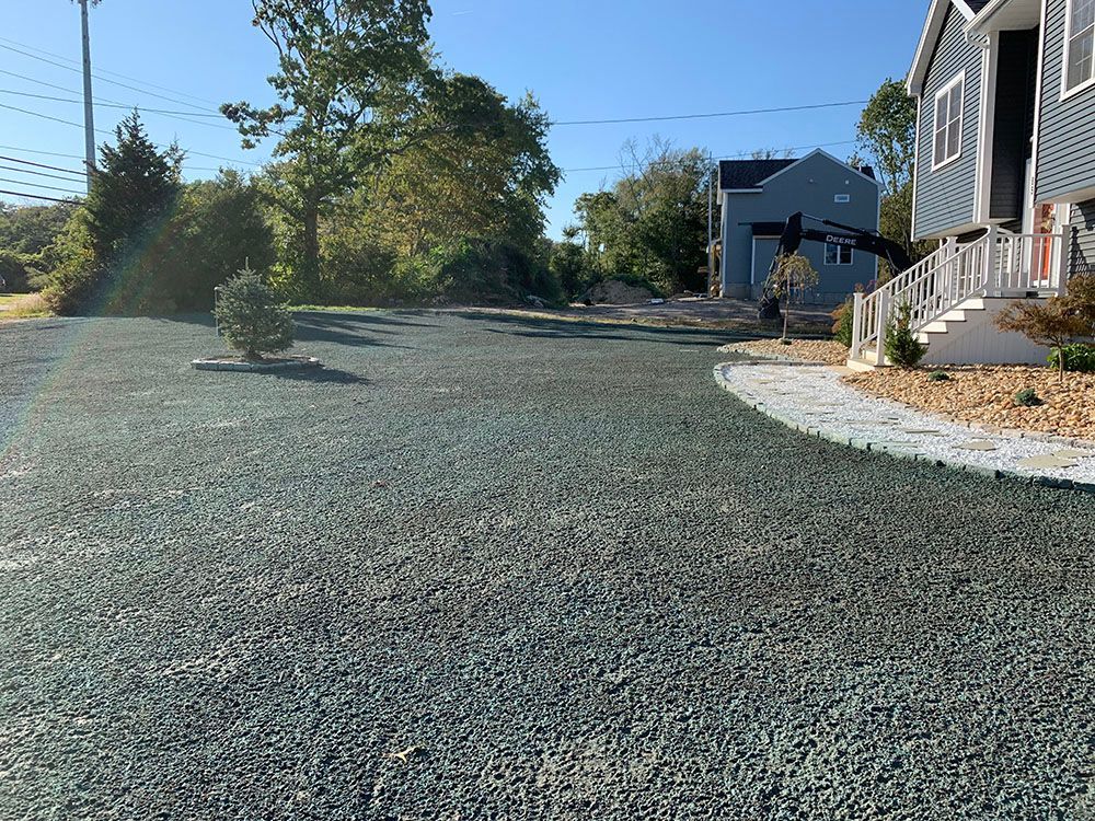 Landscape featuring gravel driveway, rock wall, and trees.