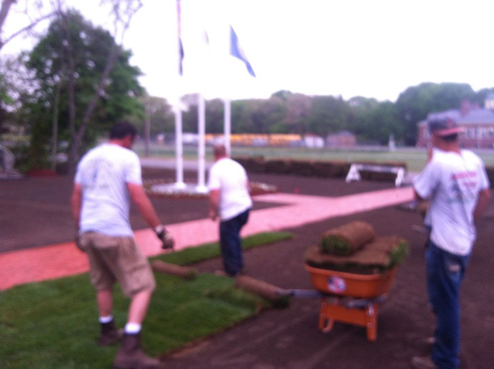Three men using a wheelbarrow to work on a lawn.
