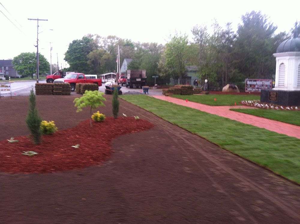 A white dome and a fountain in a park, surrounded by greenery and flowers.