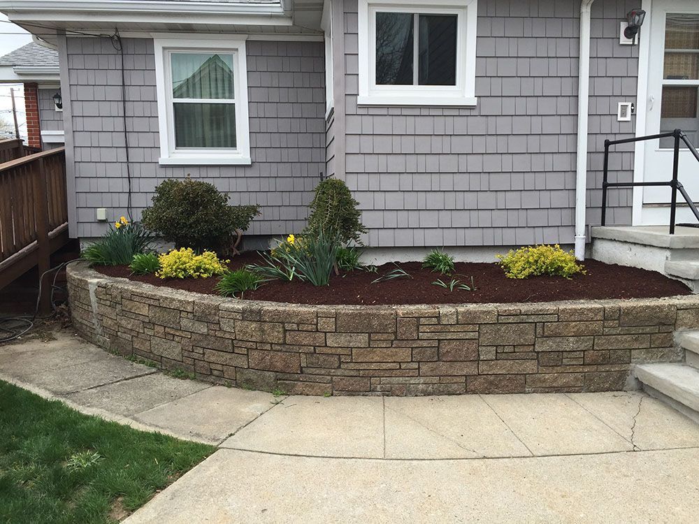 A colorful flower bed with a bench in front of a charming house.
