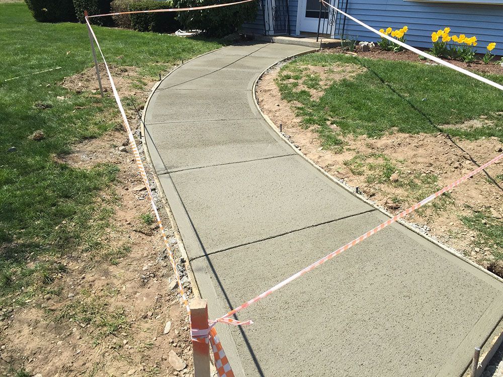 A newly constructed concrete walkway in front of a house, providing a sturdy and accessible path.
