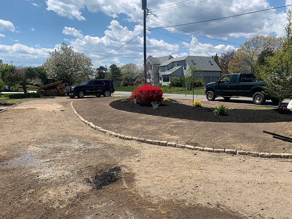 A driveway with a landscaping project in the middle. The project includes plants, flowers, and decorative stones.