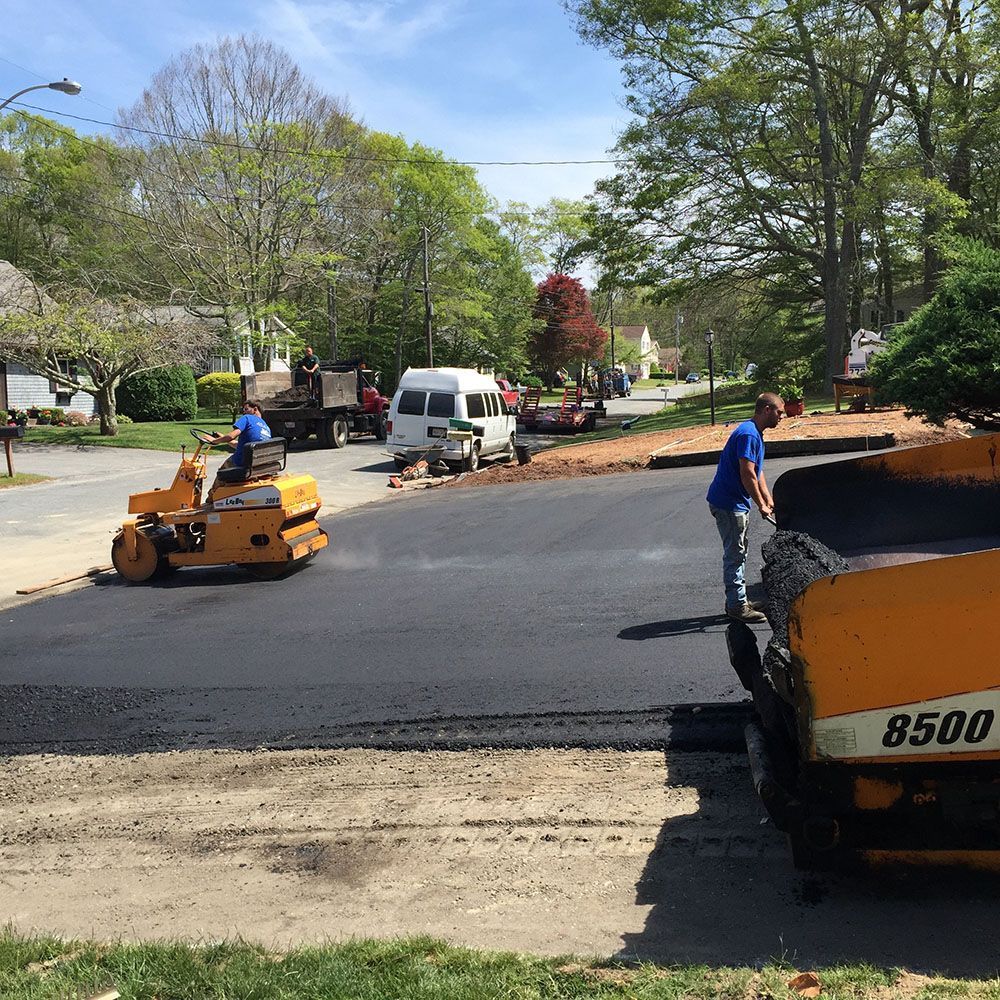 Worker using roller to pave driveway.
