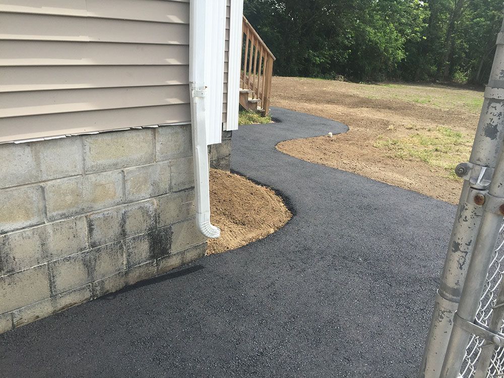 A black asphalt driveway leading to a house, providing a smooth and durable surface for vehicles.