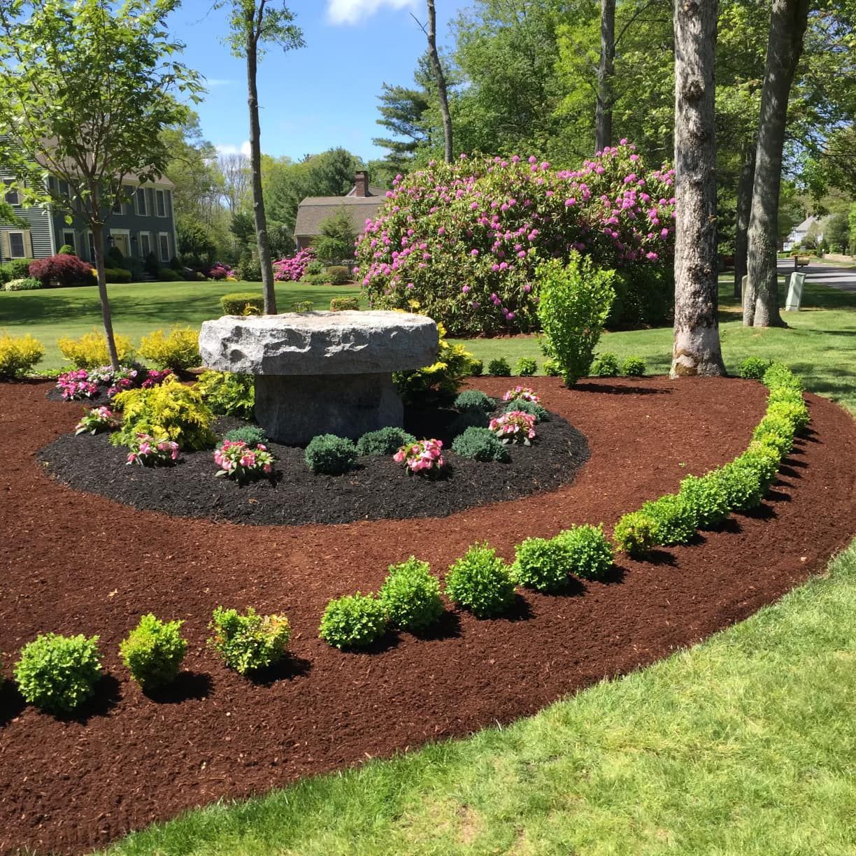 a stone bench is surrounded by flowers and mulch in a garden