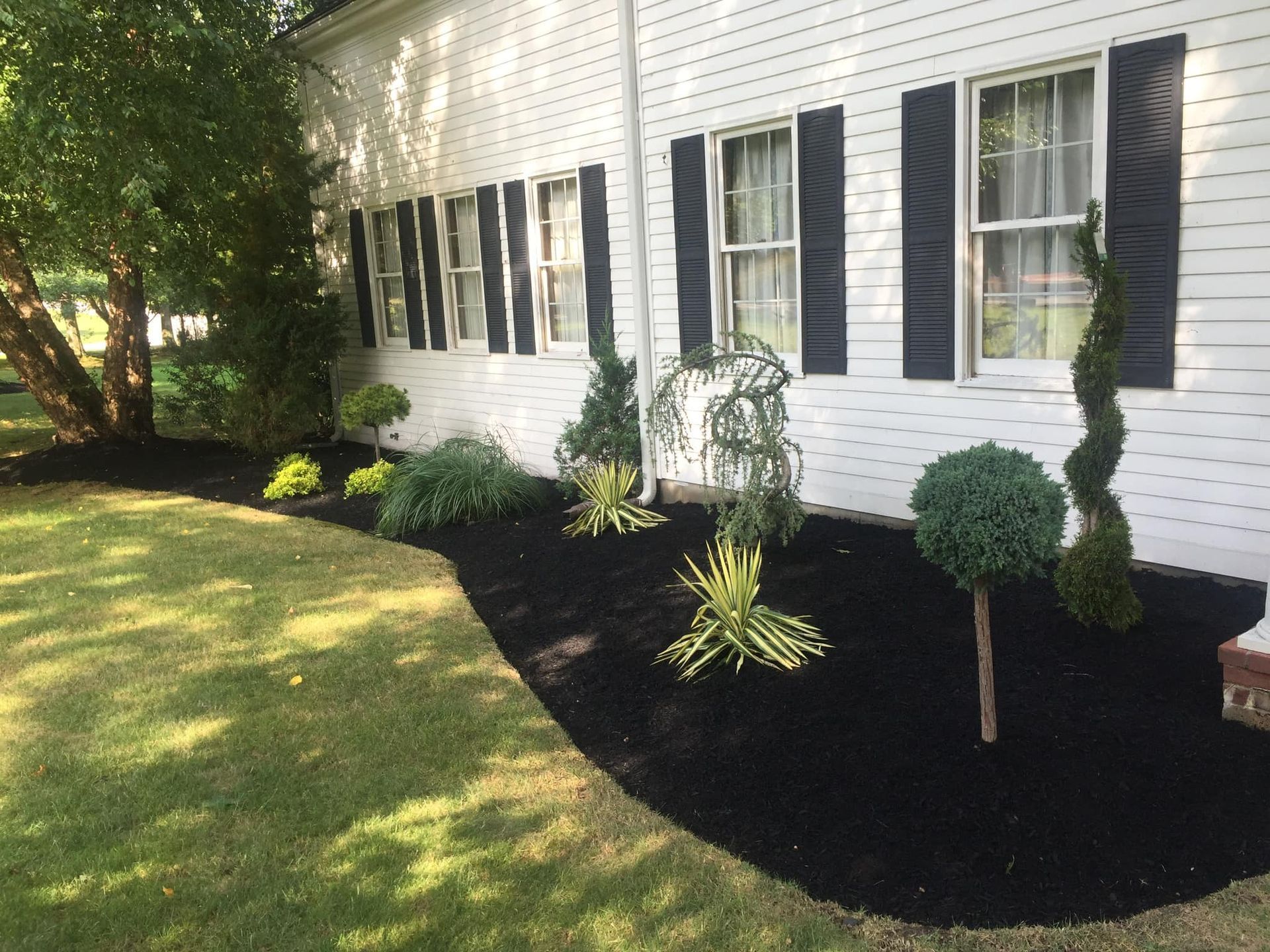 a white house with black shutters and black mulch in front of it