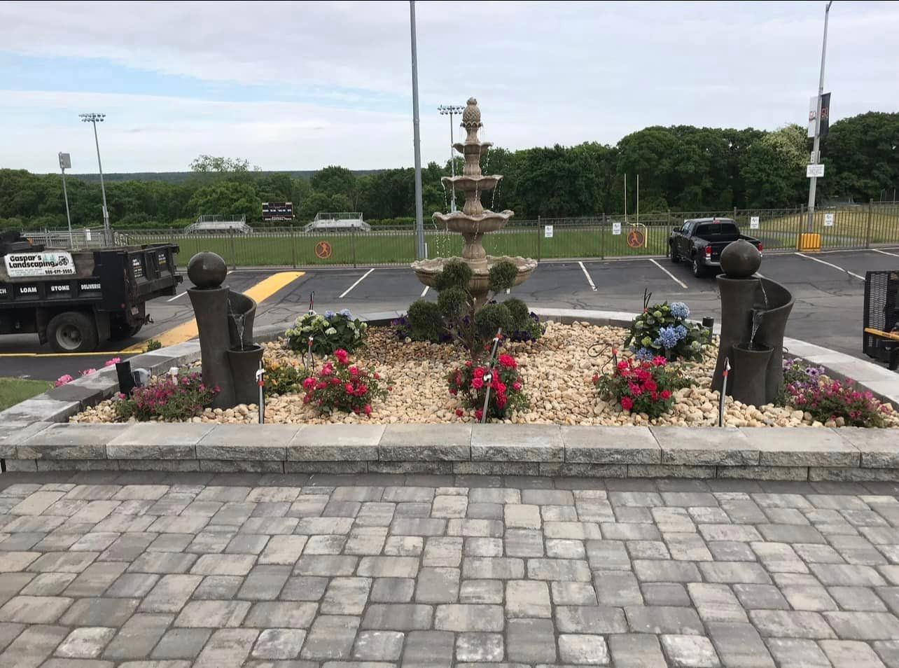a brick walkway with a fountain and flowers in the middle of it