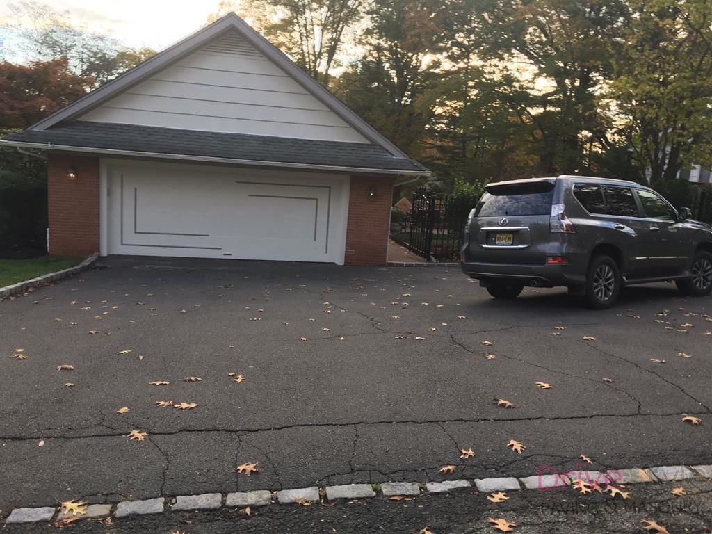 Driveway with a white garage and a dark SUV parked on the right, scattered leaves on the pavement.
