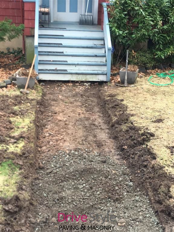 Freshly dug soil path leading up to a house porch steps with tools and hose on either side