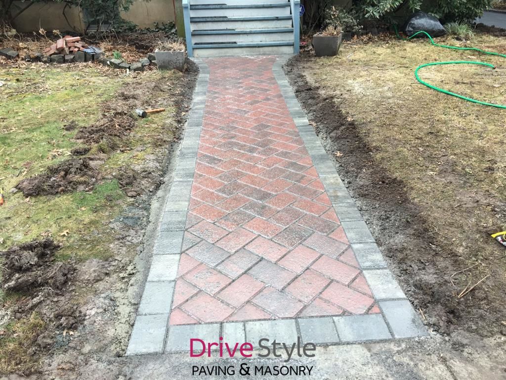 Brick walkway with gray borders leading to steps in a yard