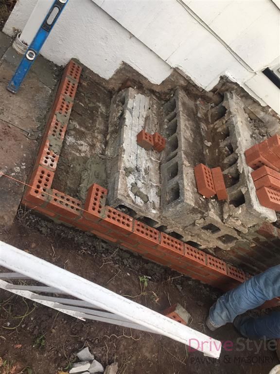 Brickwork foundation repair around a damaged concrete corner beside a white wall.