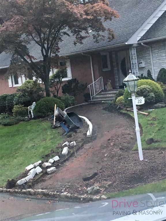 Damaged front walkway with broken curb and displaced stones leading to a brick house entrance