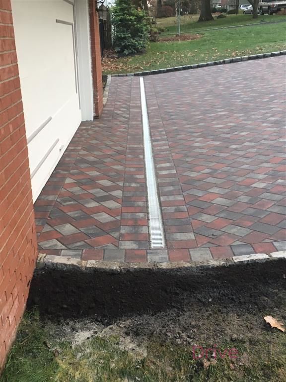 Brick driveway with a narrow concrete strip beside a garage and lawn edge