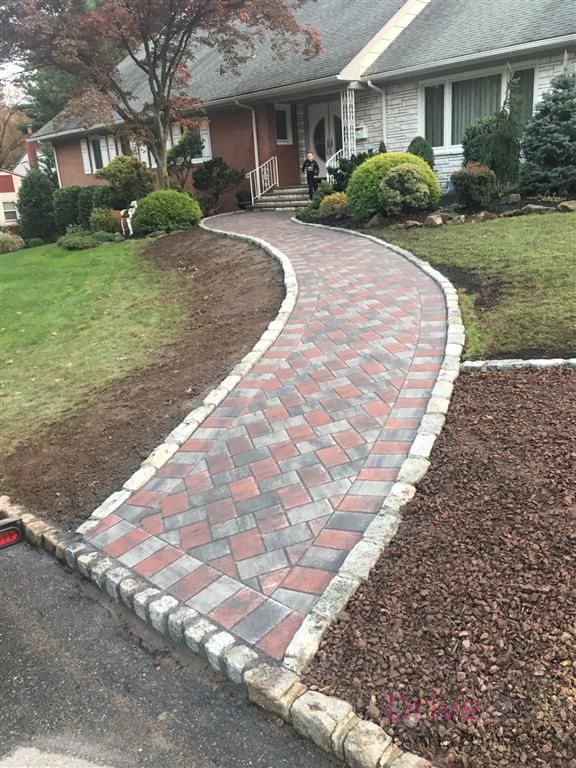 Curved red and gray brick walkway leading to a brick house with landscaped front yard