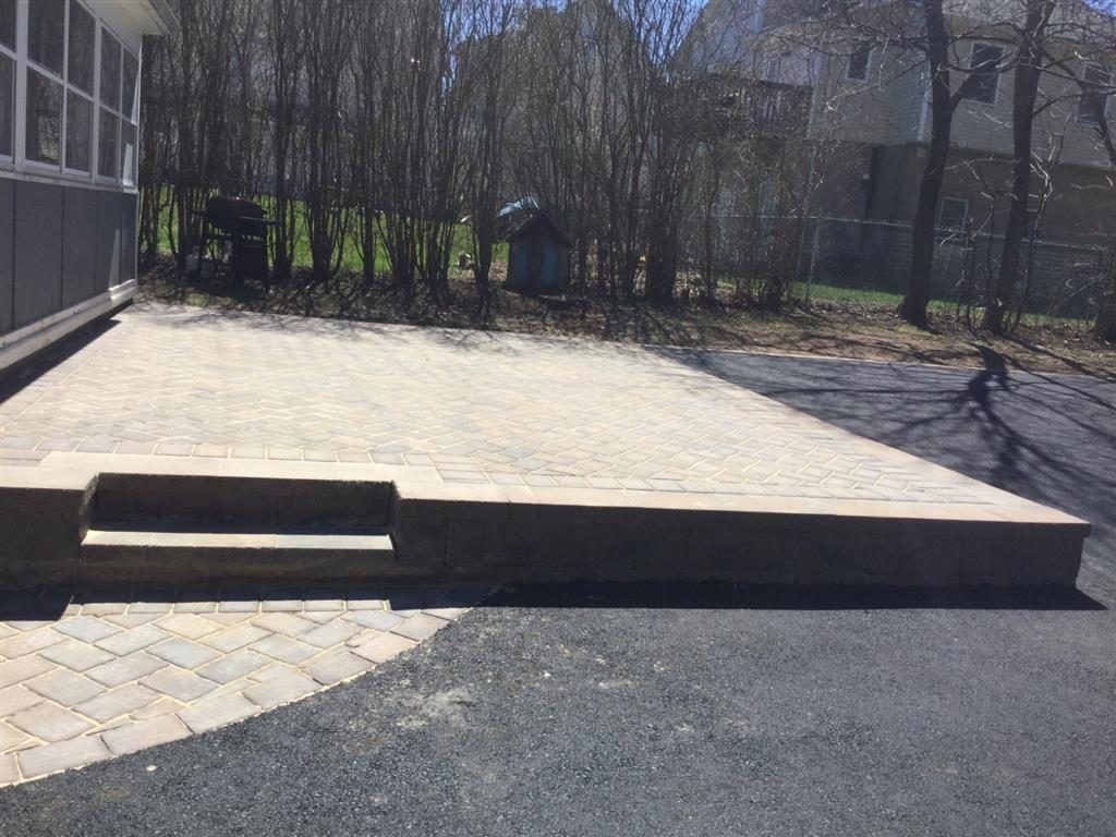 Outdoor ramp and step leading to a building entrance, with paved walkway and trees in the background.