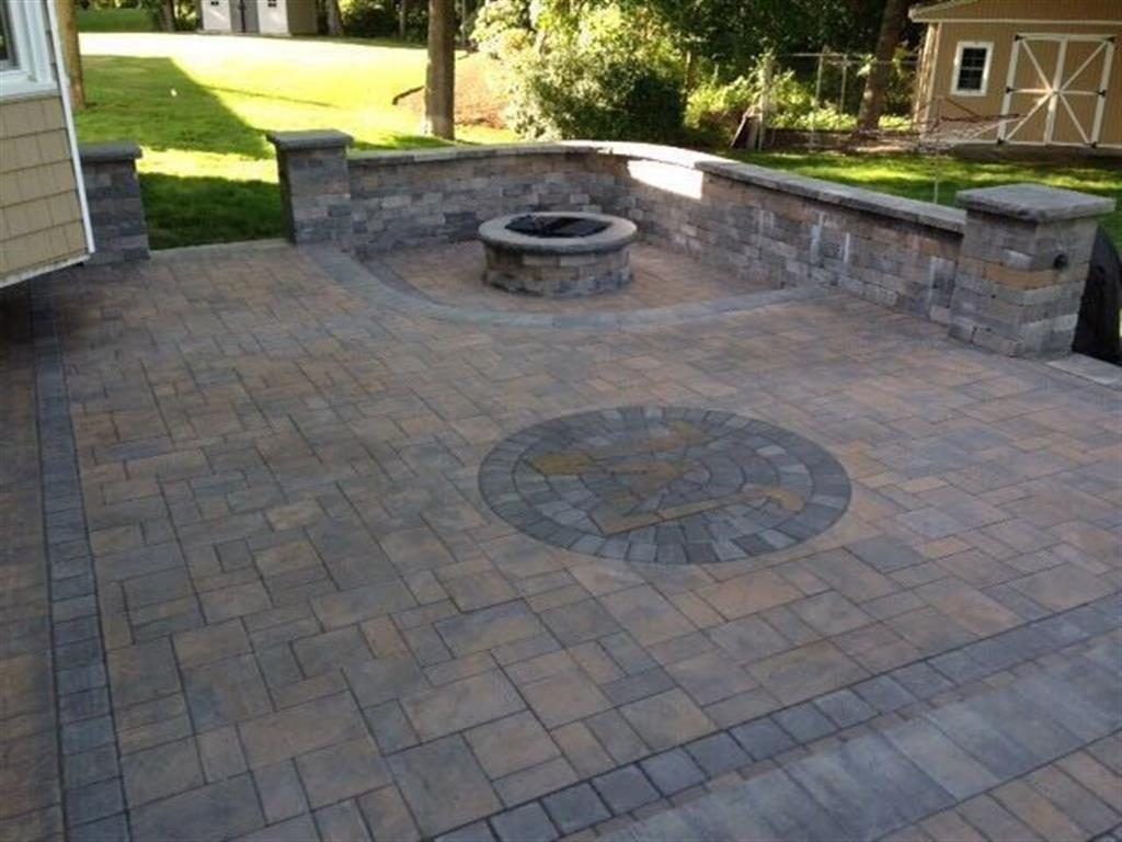 Stone patio with circular inlay and built-in fire pit, bordered by a low brick wall and lawn.