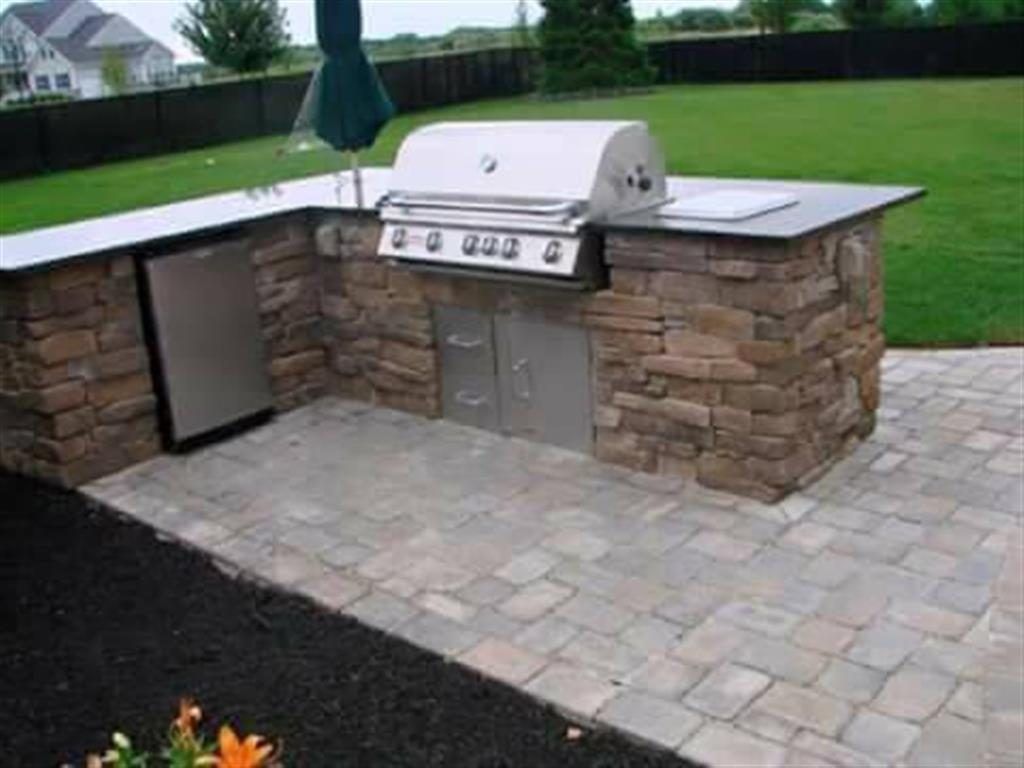 Built-in outdoor grill with stone counters and paver patio in a backyard