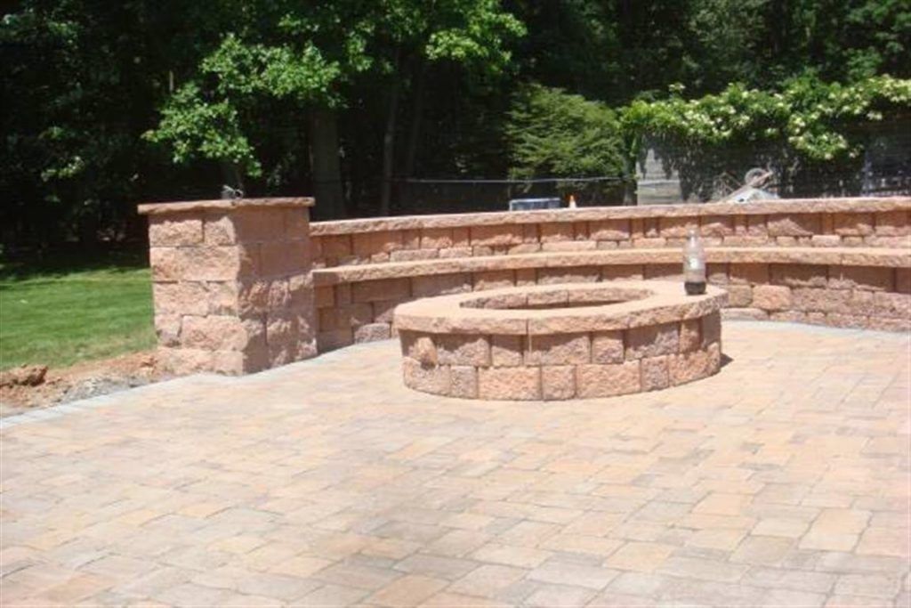Stone patio with a circular built-in fire pit and low retaining wall under trees