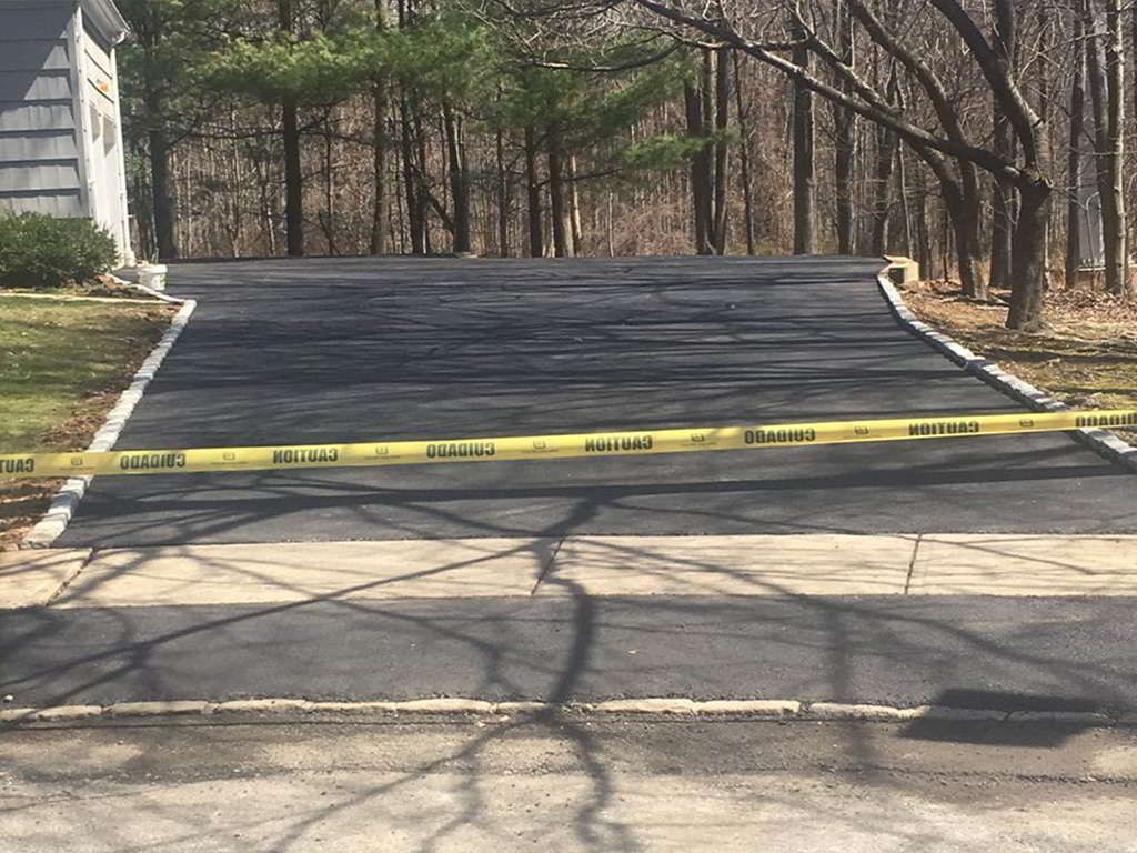 Blocked driveway with yellow caution tape across a paved entrance near trees and a house