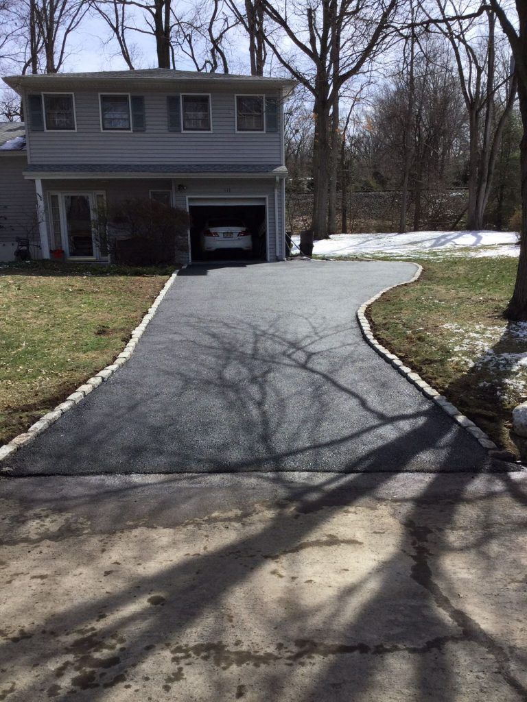 Driveway leading to a two-story house with a garage, lined by leafless trees and patchy snow.