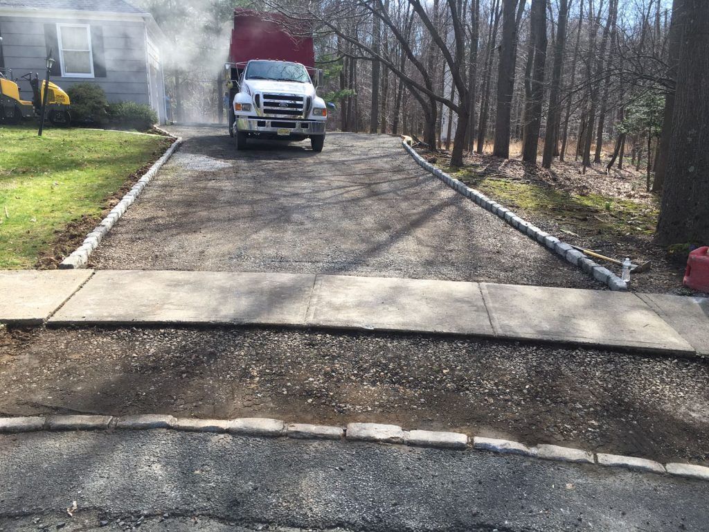 Pickup truck parked on a gravel driveway beside a house, with smoke or steam drifting from the left side.