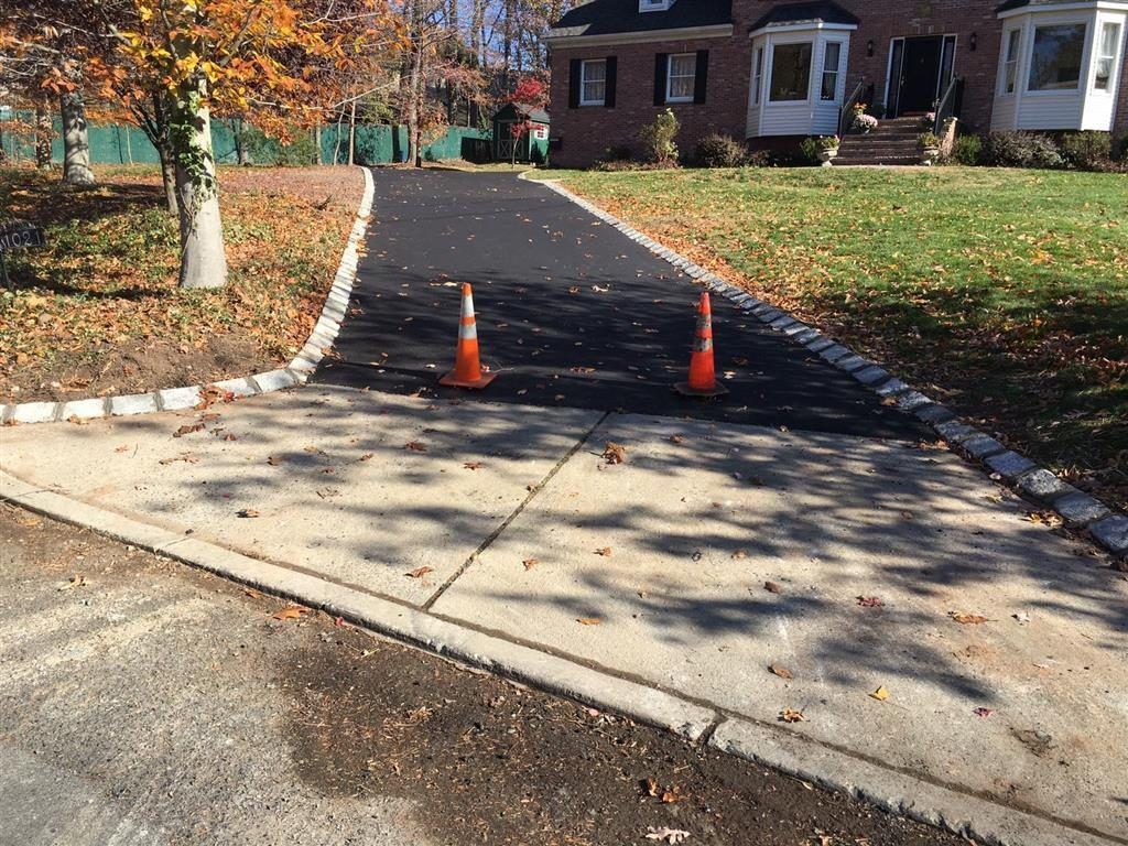 Driveway entrance with two orange traffic cones, trees, and a house in the background.