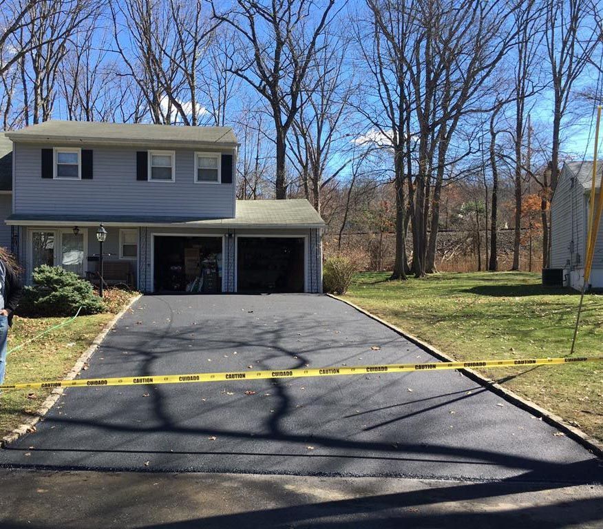Two-story house with driveway blocked by yellow caution tape on a sunny day