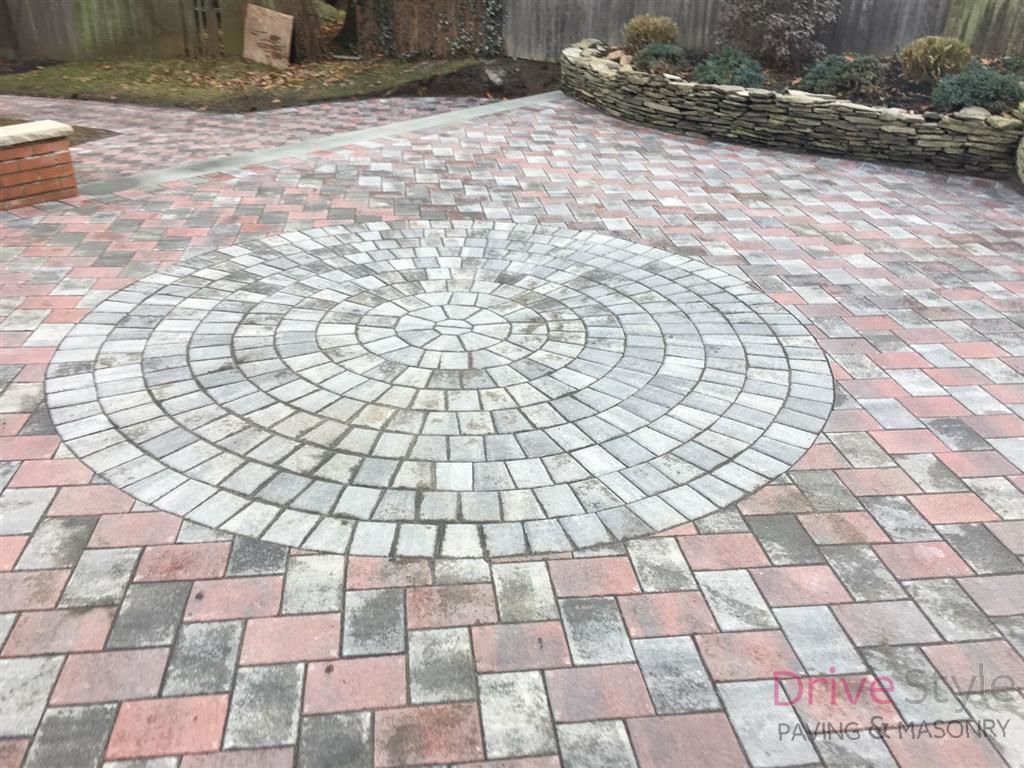 Circular stone patio with a red and gray brick pattern in a backyard