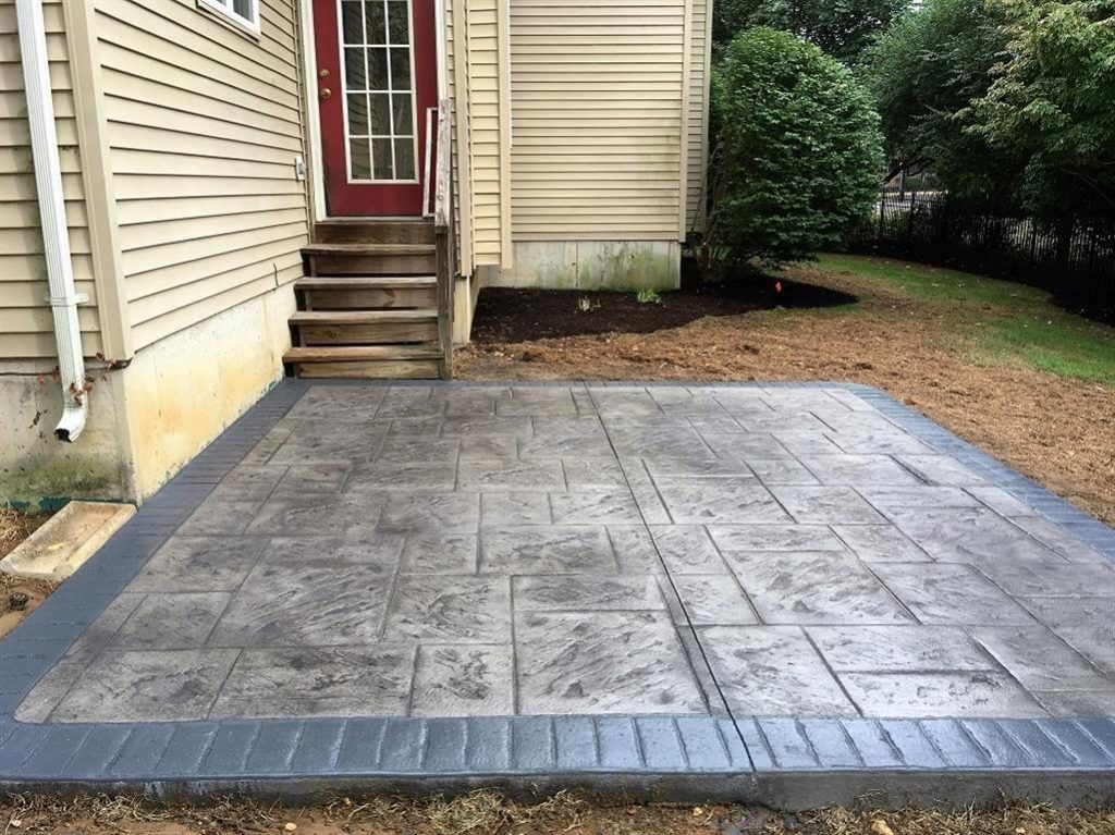 Backyard concrete patio with gray stamped surface beside beige house and steps to a red door