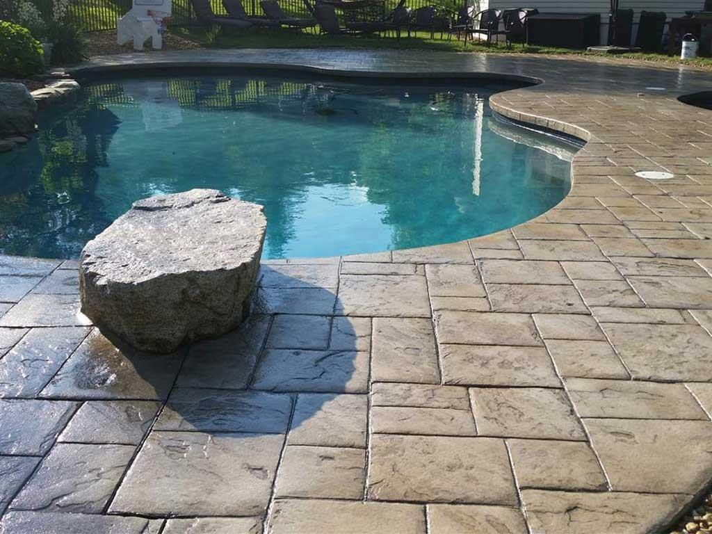 Backyard swimming pool with stone paver deck and a large rock in the foreground