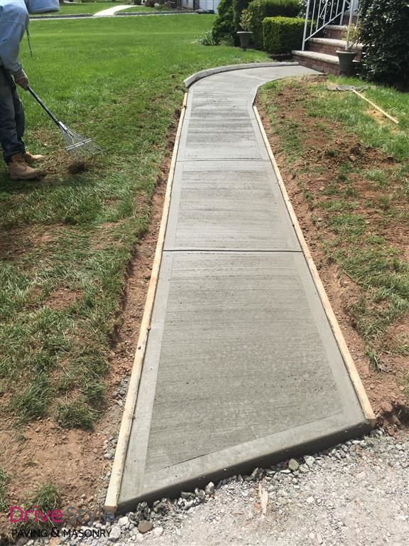 New concrete sidewalk ramp curving through a grassy yard, with a worker visible at left.