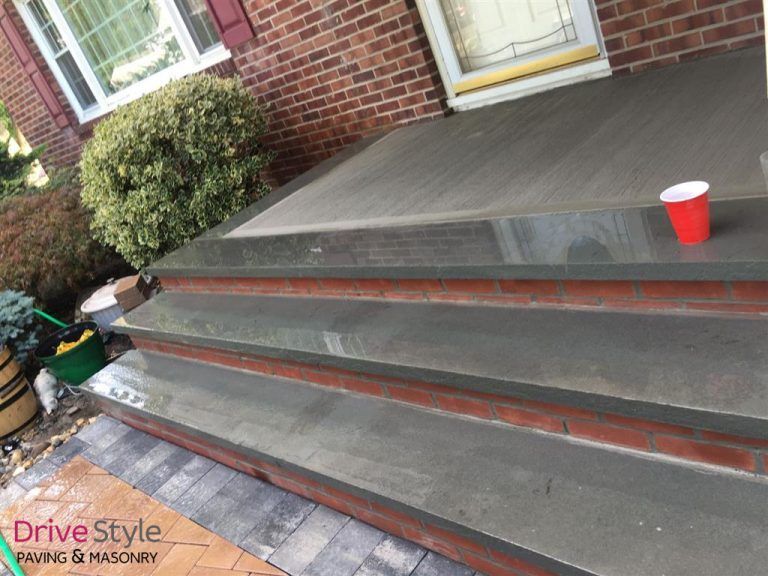Front porch with dark gray concrete steps and red trim beside a brick house, red cup on the landing